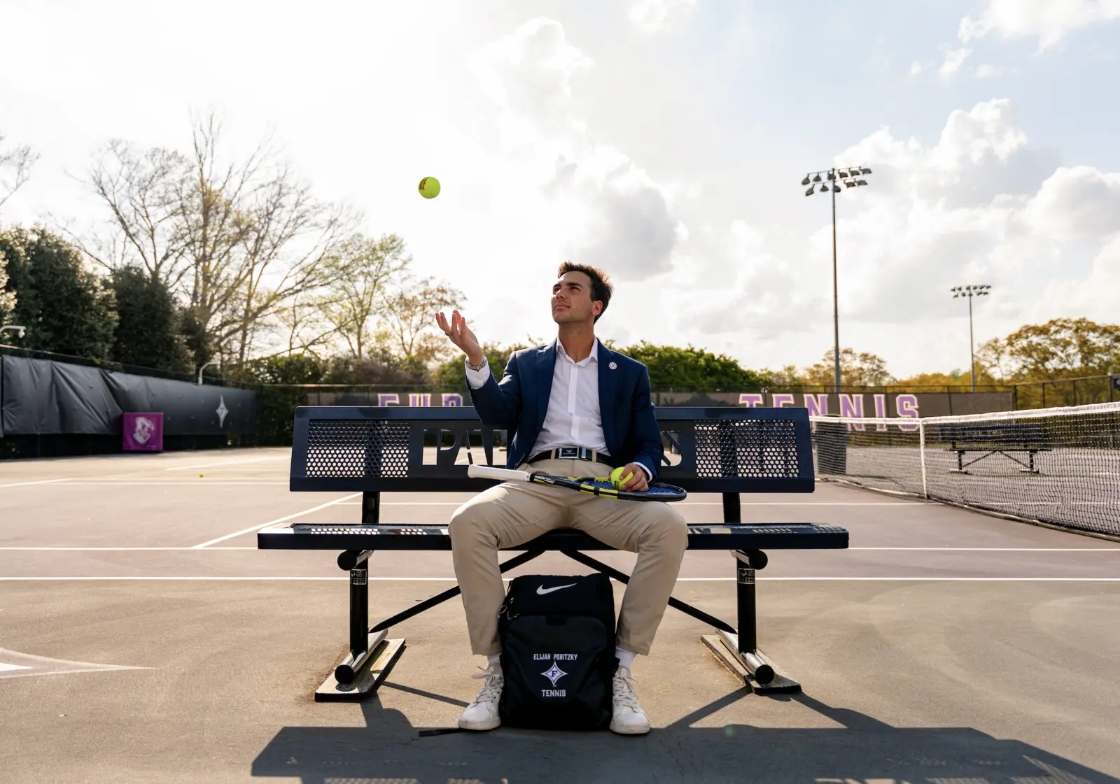 Elijah Poritzky tossing a tennis ball beside a court